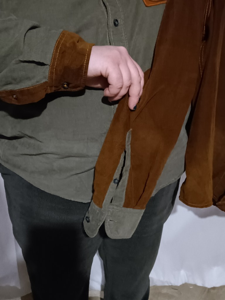 A person in a green long sleeve shirt with copper accents holding a copper long sleeve shirt with green accents.