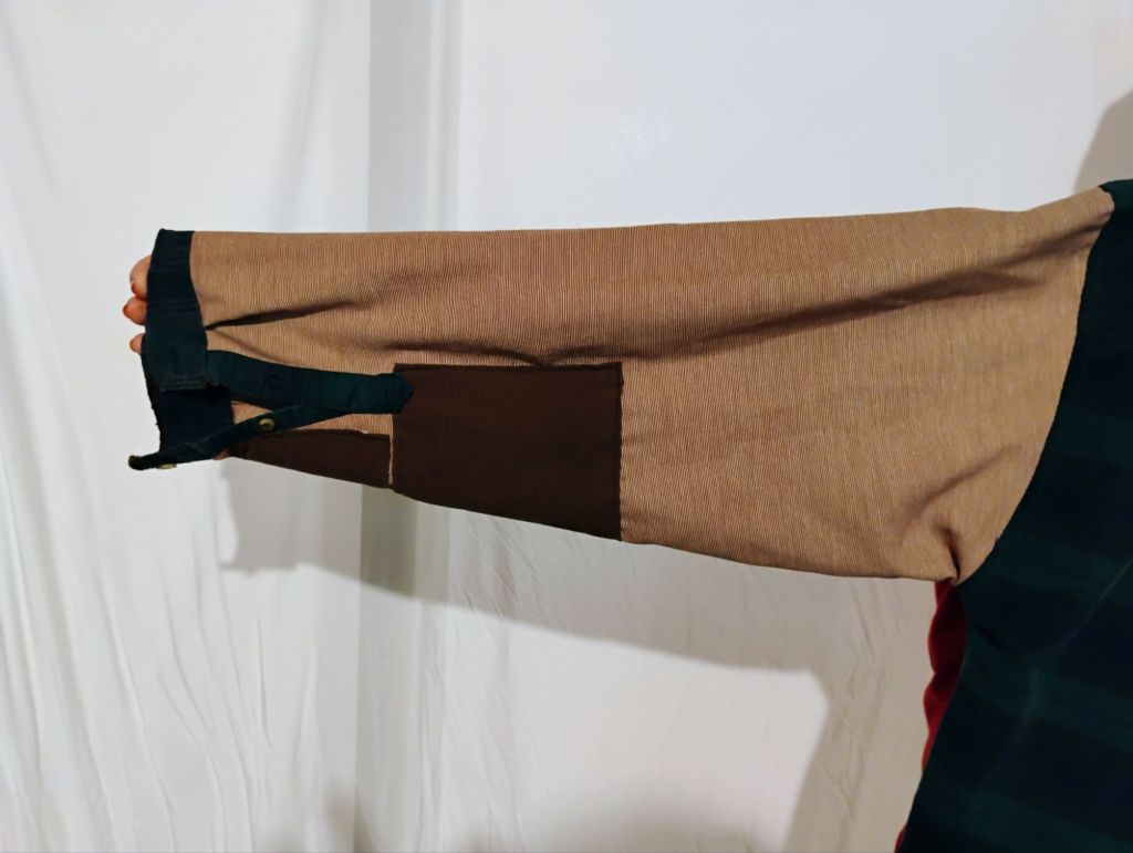 A shirt sleeve that is a pale red with green cuffs and brown elbow patch.