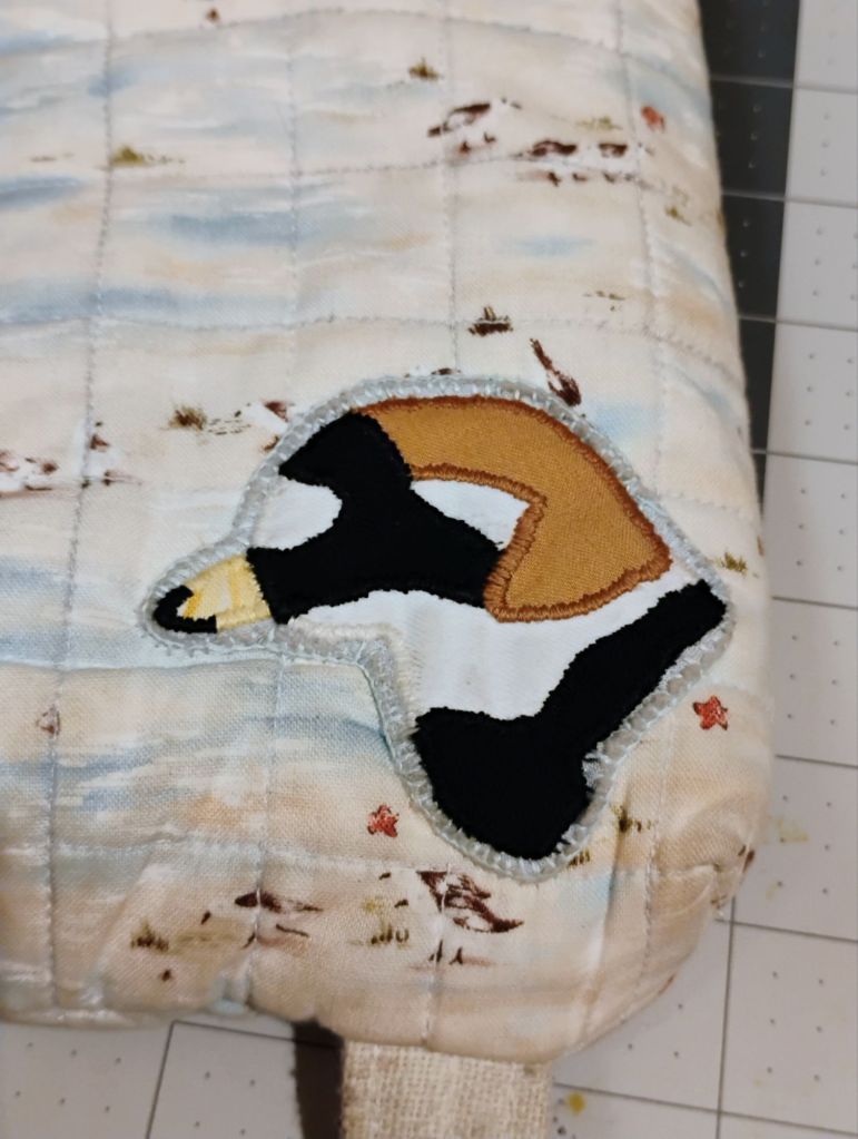 A patch of a semipalmated plover head. It is sewn onto a fabric that is tan and blue with little brown and white birds.