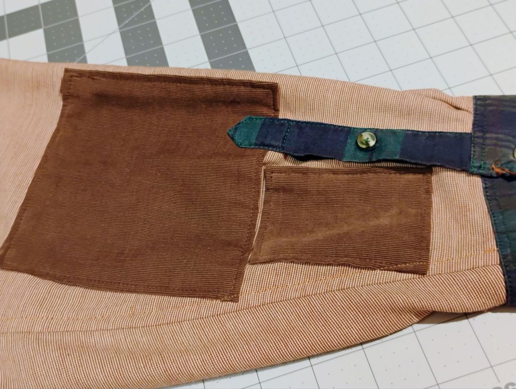 The sleeve of a pale red shirt which features two large brown rectangle patches.