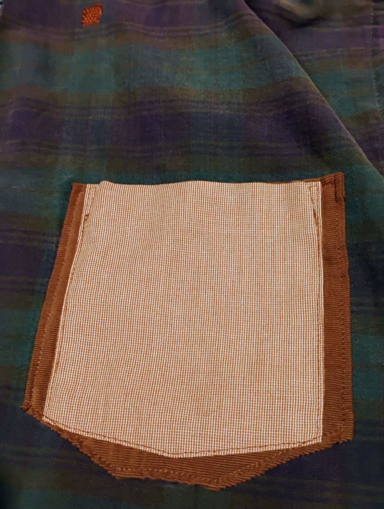 A pale red patch pocket on top of a brown patch which is on top of a green and blue plaid fabric.