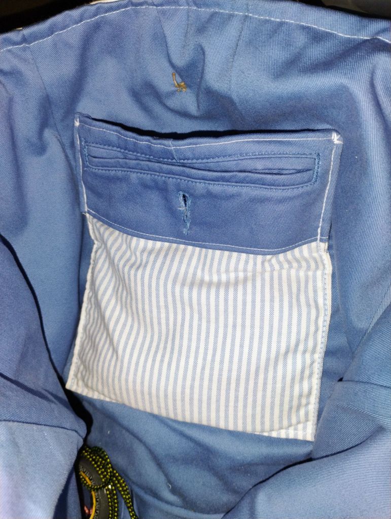 The inside of a bag lined with blue. It has a striped pocket made from a back pants pocket.